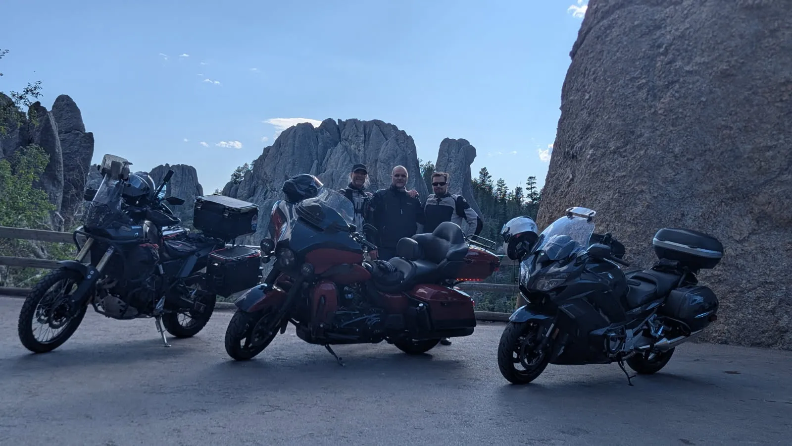 Three touring motorcycles parked at a rocky mountain overlook, three riders standing together behind them.